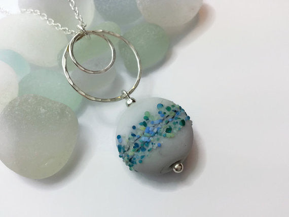 Sea blues, greens and grey lampwork glass bead and sterling silver hammered circles necklace.